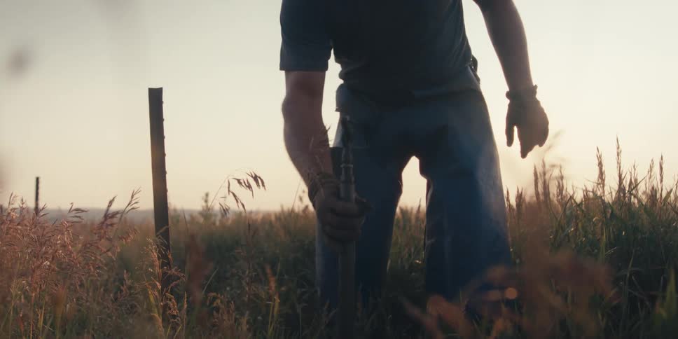 Man working in a field and picks up a large metal tool