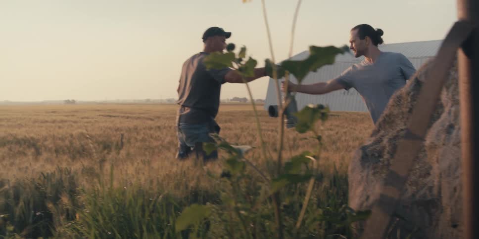 A worker on a farm hands a piece of pipe to another man