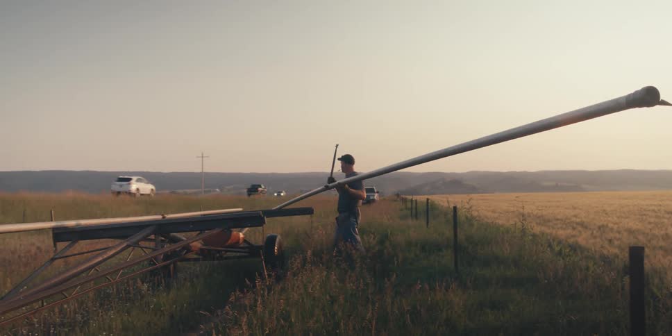 A farmer gathers irrigation pipe from a field on the side of a road