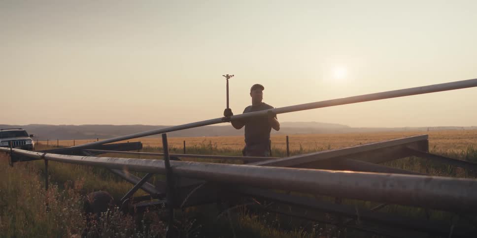 A worker on a farm is carrying irrigation pipe from a field