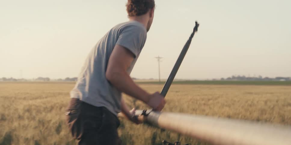 A farmer in a grain field picks up an irrigation pipe to move it