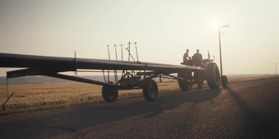 The two men are on the tractor and the tractor is pulling some type of farming equipment