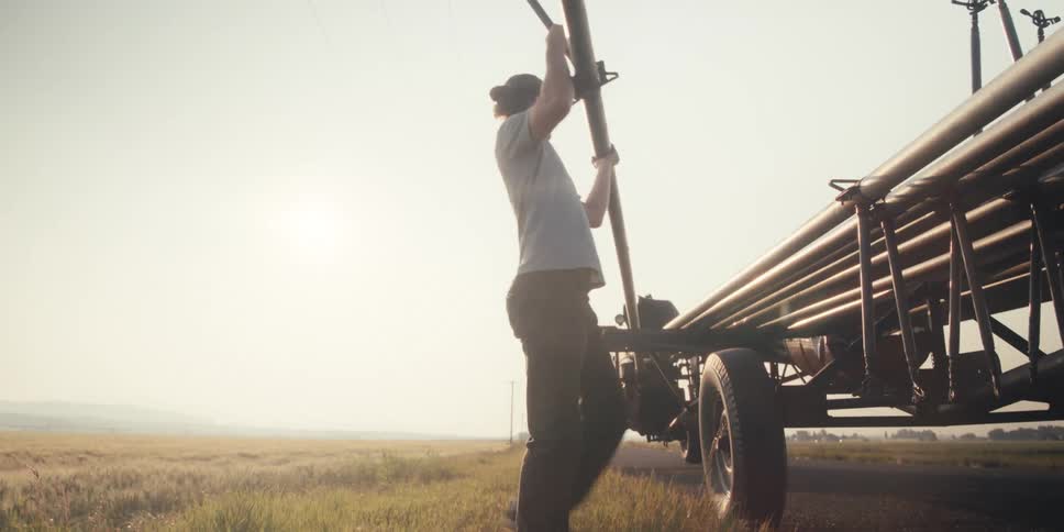 A man is moving irrigation pipes onto a trailer on a farm