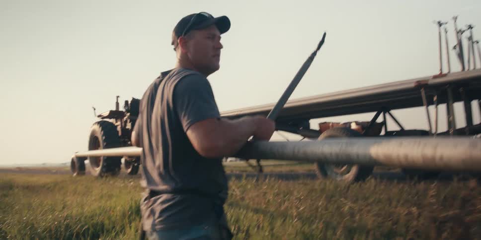 Man working carrying an aluminum pipe from a wheat field