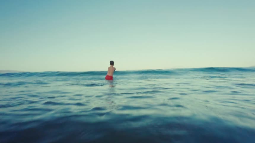 Boy with a red swim trunks walks into the ocean with the waves