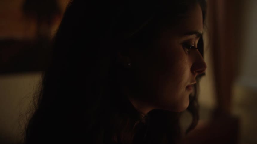 A woman stares outward in a dark room
