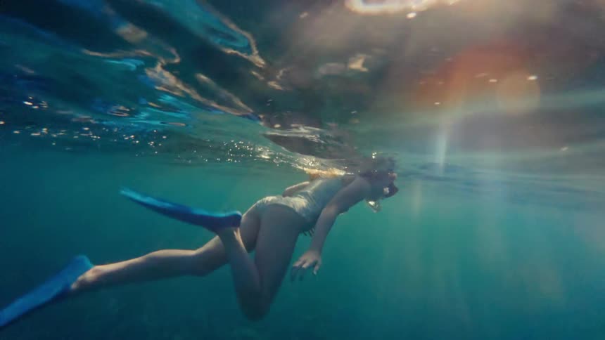 A girl wearing blue fins is snorkeling while at the beach