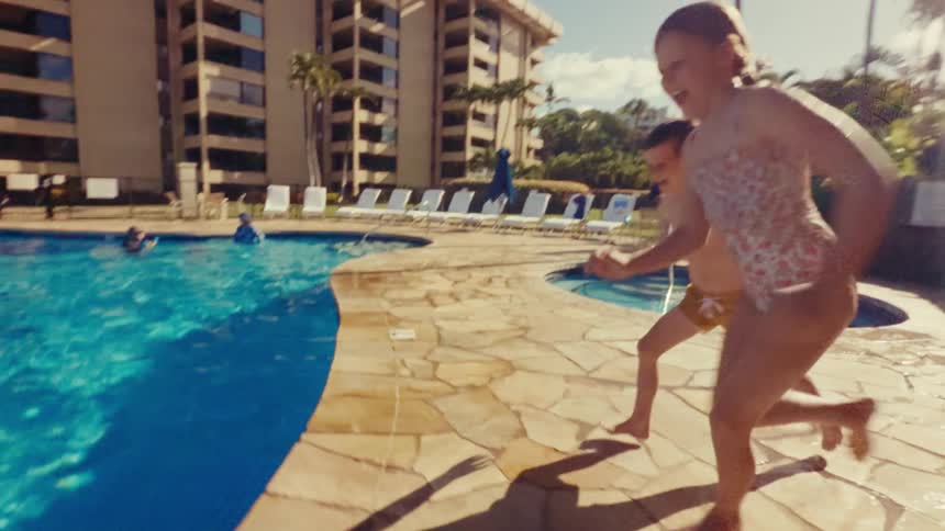 A boy and girl jump into a pool on a sunny day during a hotel vacation