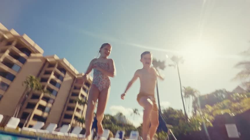 A boy and girl run and jump into a pool splashing water into the air