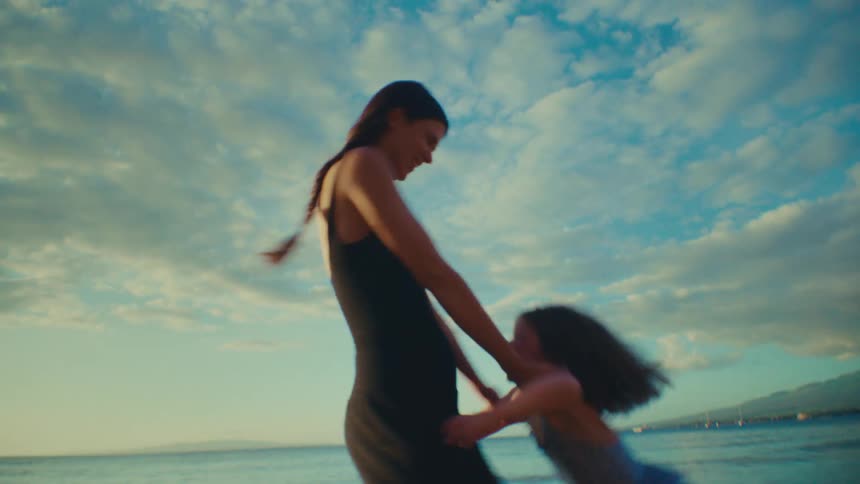 A mother is spinning her child around in the air at the beach
