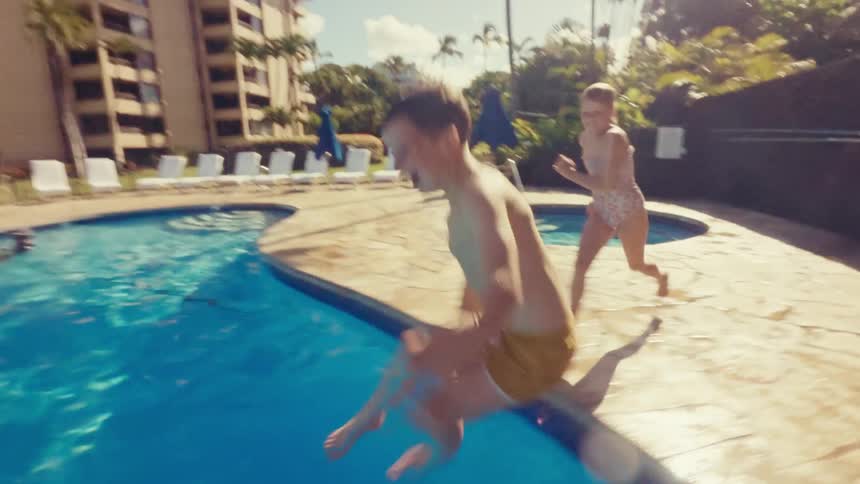 A boy and girl jump into a pool on a sunny day during a hotel vacation