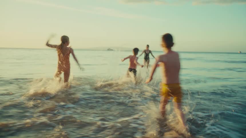 Children running on the beach to the sea and mother