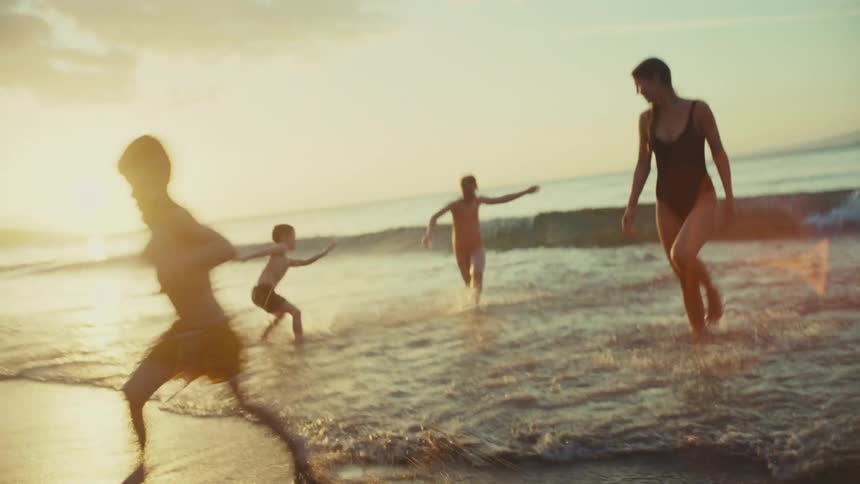 A woman and three children playfully run through the shallow waves on a sundrenched beach
