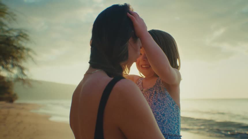 A mother holds her happy toddler daughter on the beach near the ocean