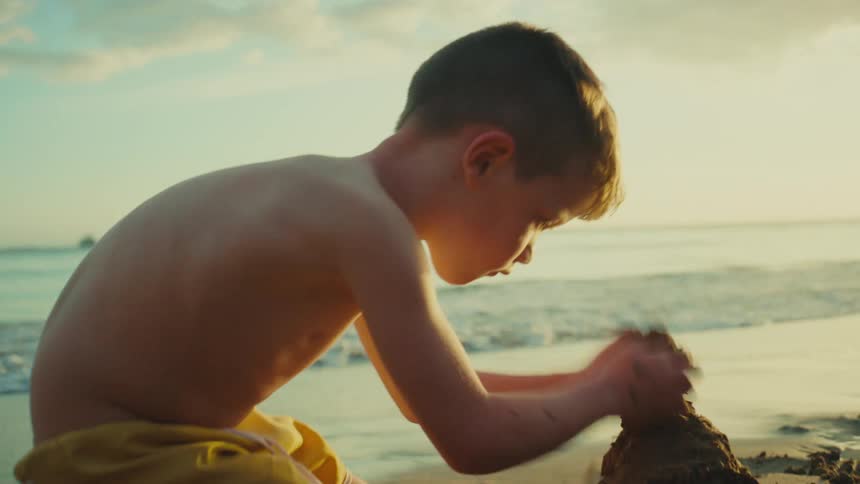 Two children are playfully building a sandcastle near the waters edge during a golden hour sunset