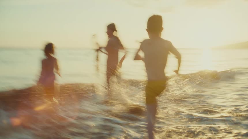 A group of children running towards the ocean waves on a sandy beach at sunset with a golden light illuminating the scene