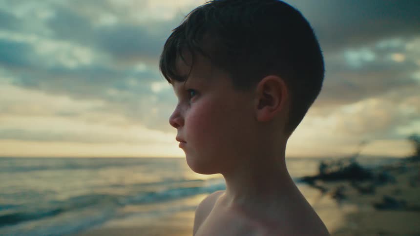 A boy is looking out onto the ocean from the beach