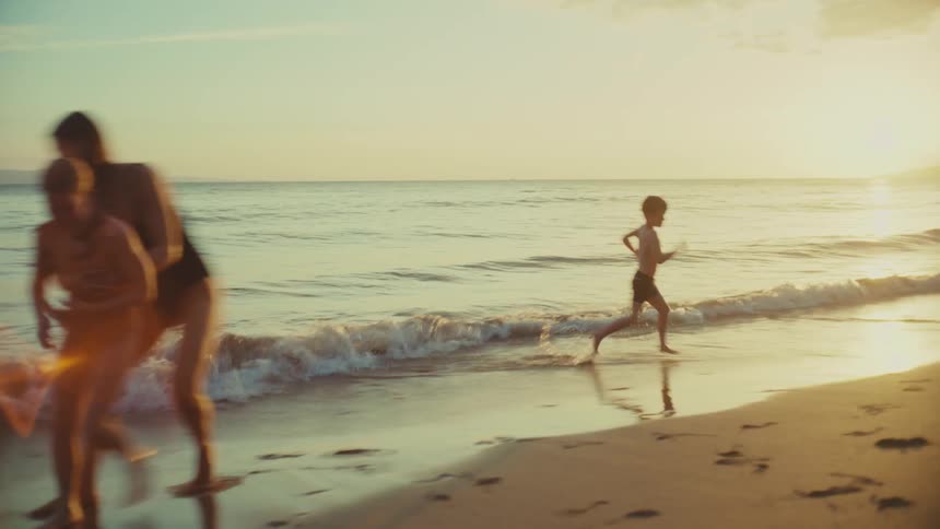 Mother and kids running and playing on shoreline at the beach at sunset