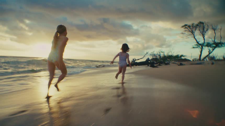 Two girls run across wet sand at the beach near driftwood enjoying a funfilled sunset by the coast