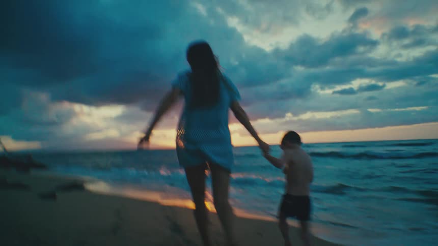 A mother and son run down the beach in the evening