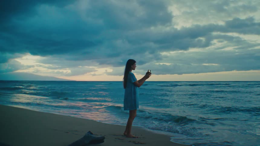 A woman takes a photo of the ocean with her cell phone