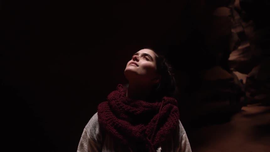 A woman standing in a dark cavern is looking up