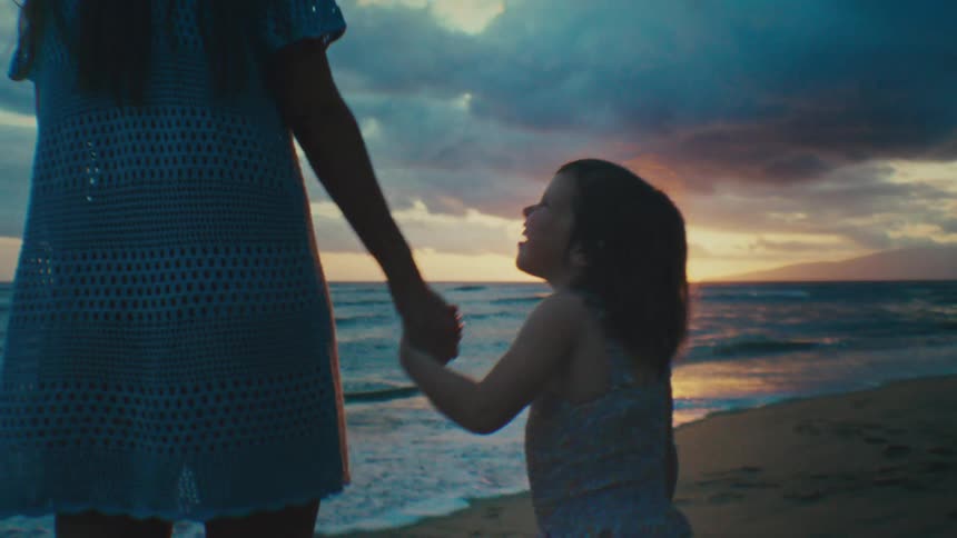 Daughter holds hands with mother on a beach at sunset