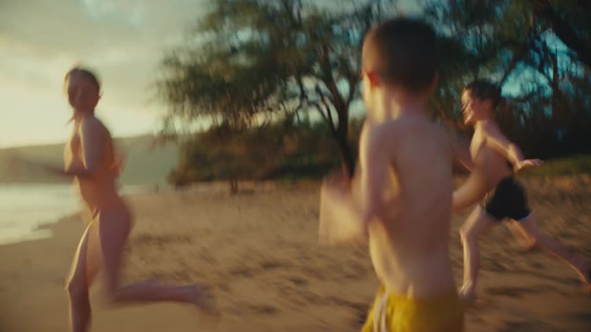 Two boys and two girls are running into the water at the beach while a woman is watching from the water