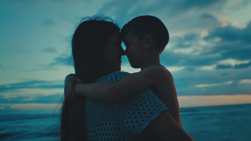 The mother is hugging her son at sunset in front of the ocean