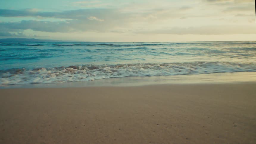 A serene beach scene shows gentle waves rolling onto a sandy shore under a cloudy sky