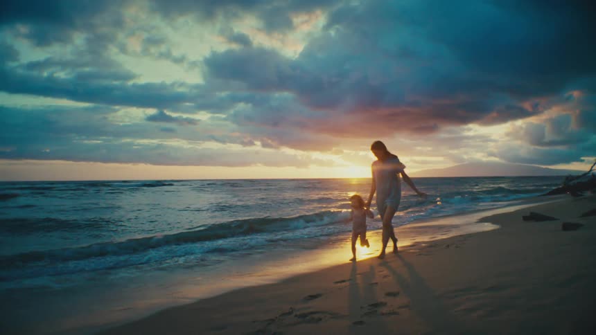 Mother and daughter running along the shoreline at sunset