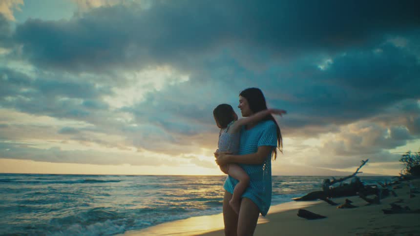 Mother spins with her daughter while enjoying the beach on a cloudy day near sunset