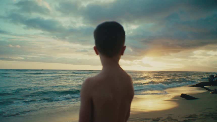 Young boy standing next to the shoreline watching the sunset