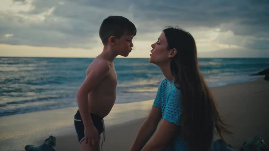 A mother kisses her son on a cloudy evening at the beach