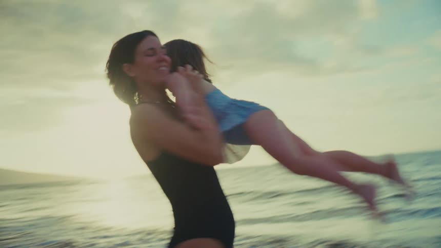 A mother picks up her daughter on the beach and spins around