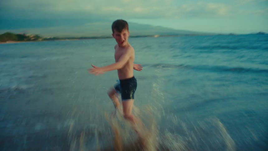 Boy excitedly runs through shallow water at the beach
