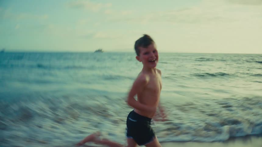 The sun is low in the sky as a boy runs along the waters edge on a beach