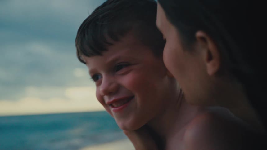 Son and mother at the beach with the child laughing as the mother leans in close creating a warm and intimate scene