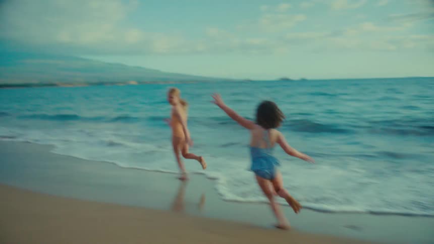 Three children are running and laughing while playing at the beach near the water