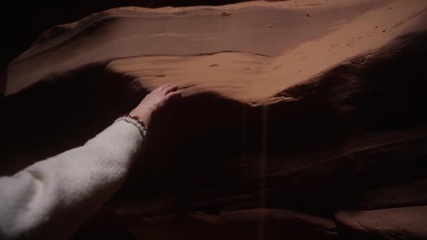 A woman rubs her hand along a large red rock