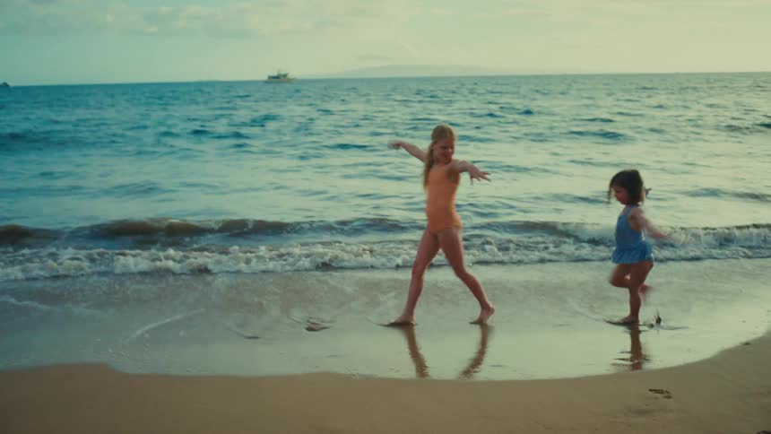 Girls in swimsuits dance on wet sand by the coast at sunset