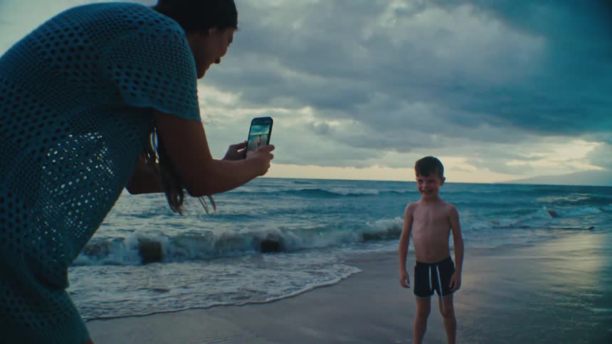 Mother taking picture of son with cellphone on the shoreline at sunset at the beach