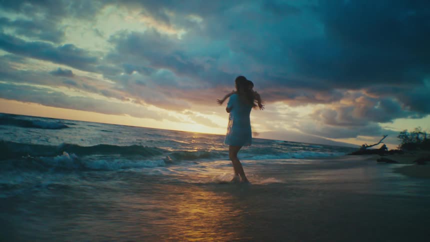 A mother is holding her daughter in her arms as she is spinning on the beach with her feet in the water