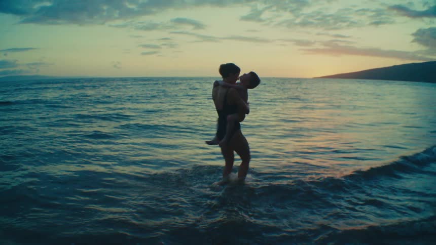 Mother spinning young son in her arms along tropical beach at sunset