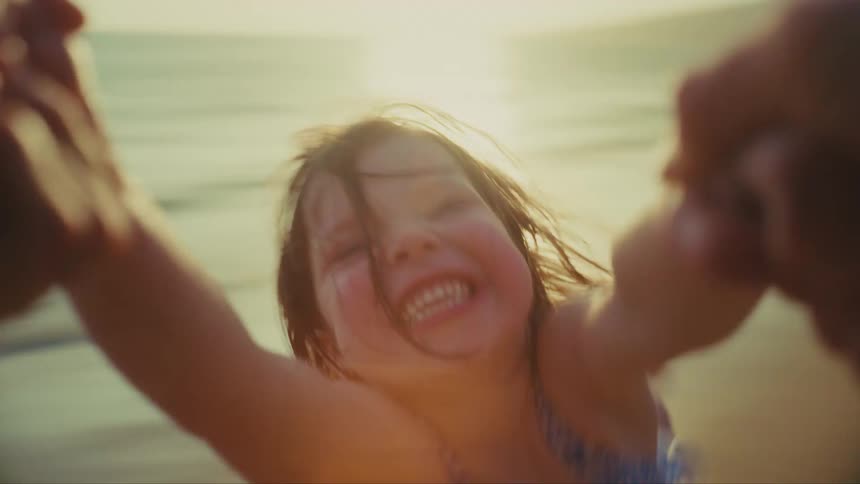 Point of view of laughing child being spun around by the arms next to the ocean