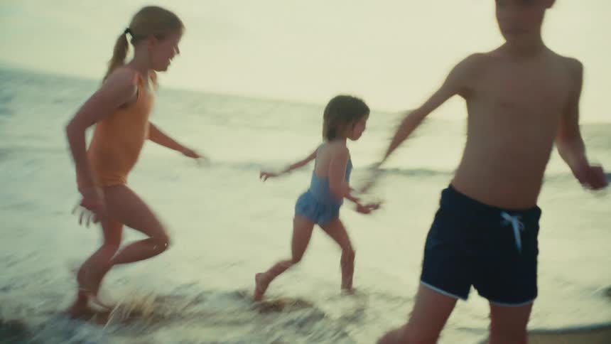 Kids smile while running in and out of the surf on a summer afternoon