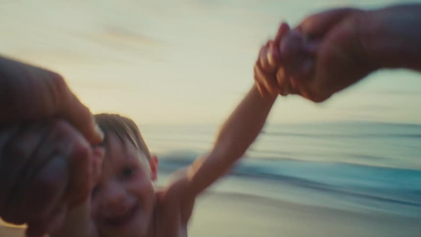 POV of parent spinning young son by his hands on tropical beach at sunset