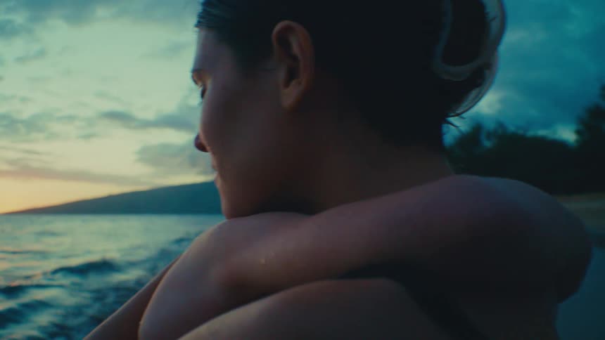 Mother gently rocking young son in her arms on tropical beach at sunset