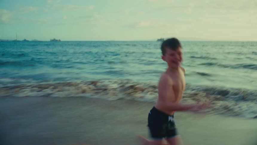 Young boy running full speed along tropical beach at sunset