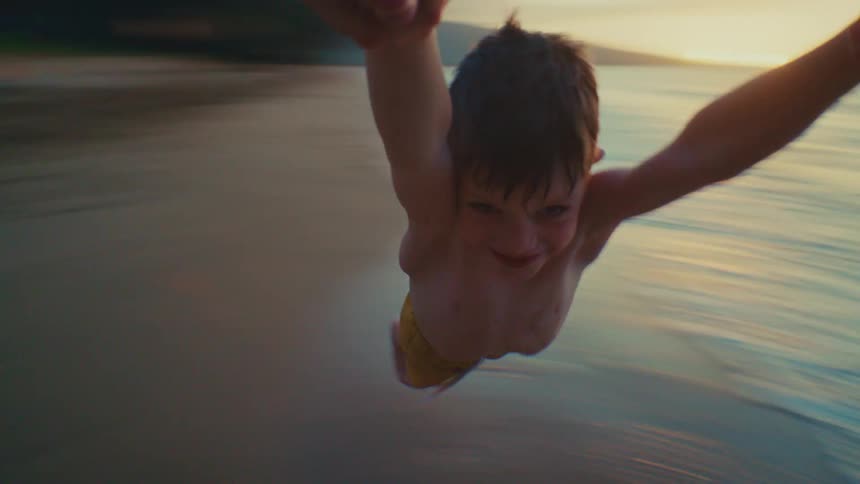POV of parent spinning smiling young son by his hands on tropical beach at sunset